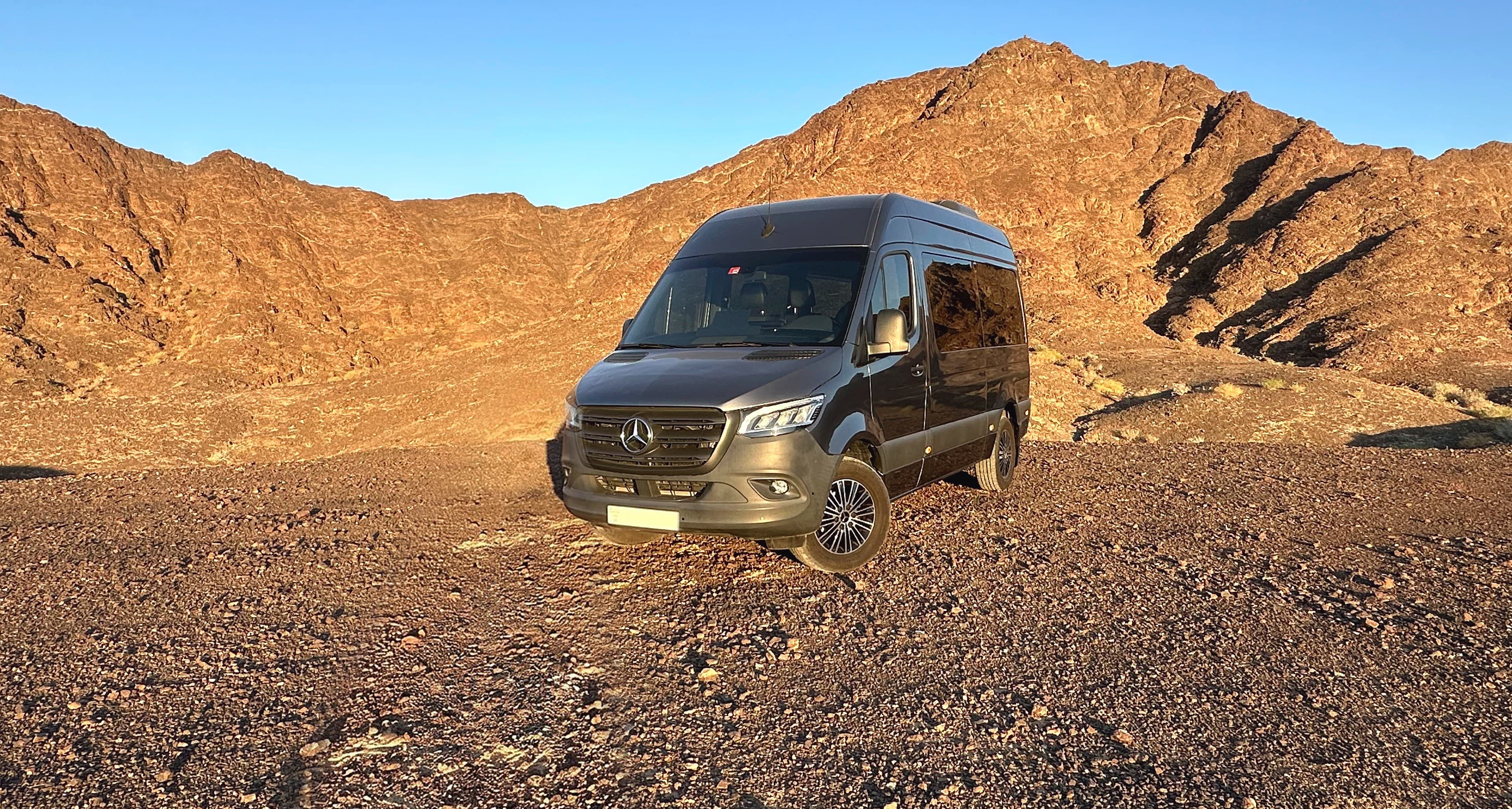 TFSL's grey Mercedes Sprinter, high roof, parked on the Hatta road with the mountains behind it